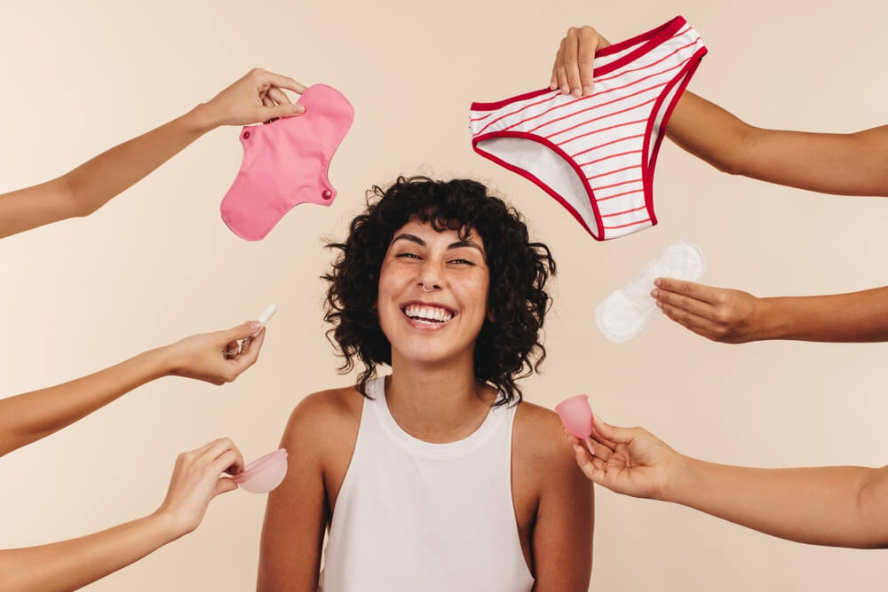 Making the Right Feminine Hygiene Choice. Happy Young Woman Smiling at the Camera While Surrounded by Hands Holding Different Disposable and Non-disposable Sanitary Products.