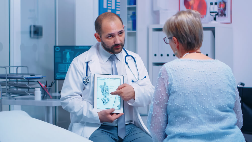 Old Woman Getting Medical Advice About Osteoporosis Bones Disease From Experienced Doctor in Private Clinic Sitting on Hospital Bed.