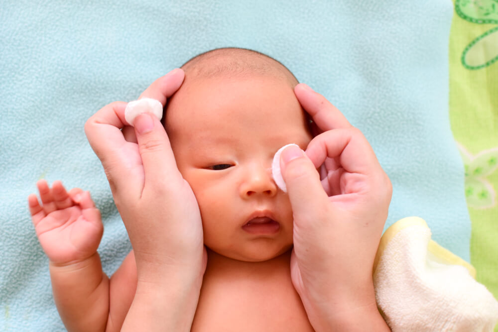 Mom cleaning baby eyes with care by wet and clean cotton