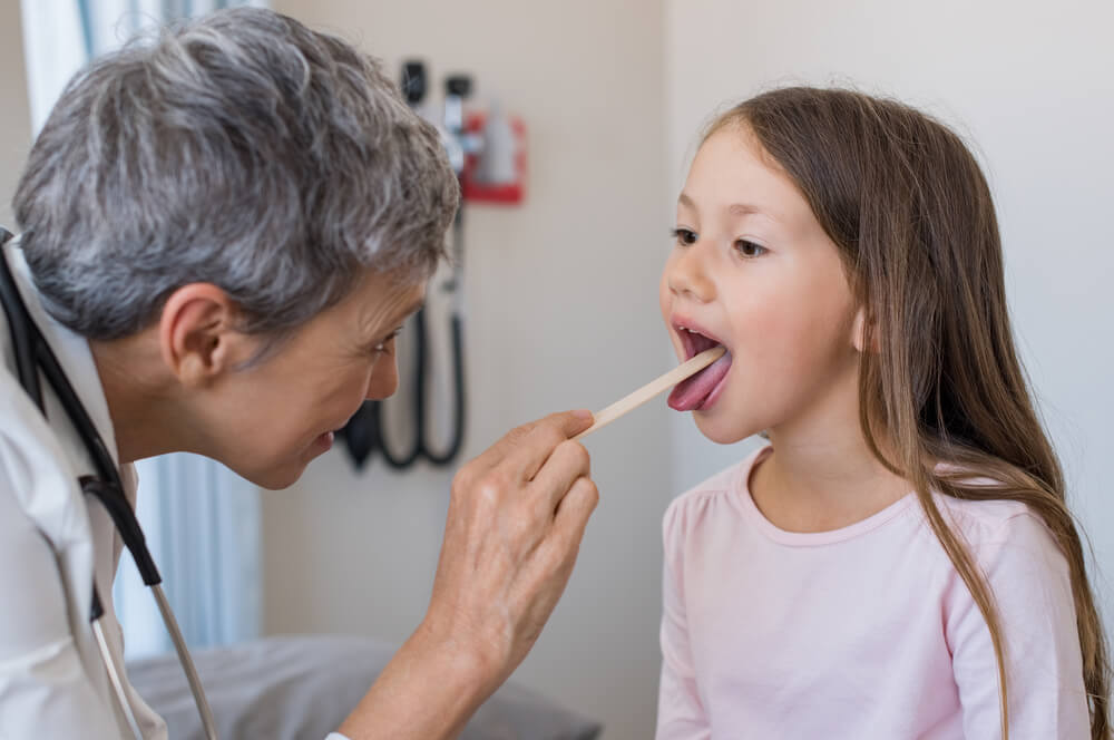 Woman doctor examining little girl mouth at office