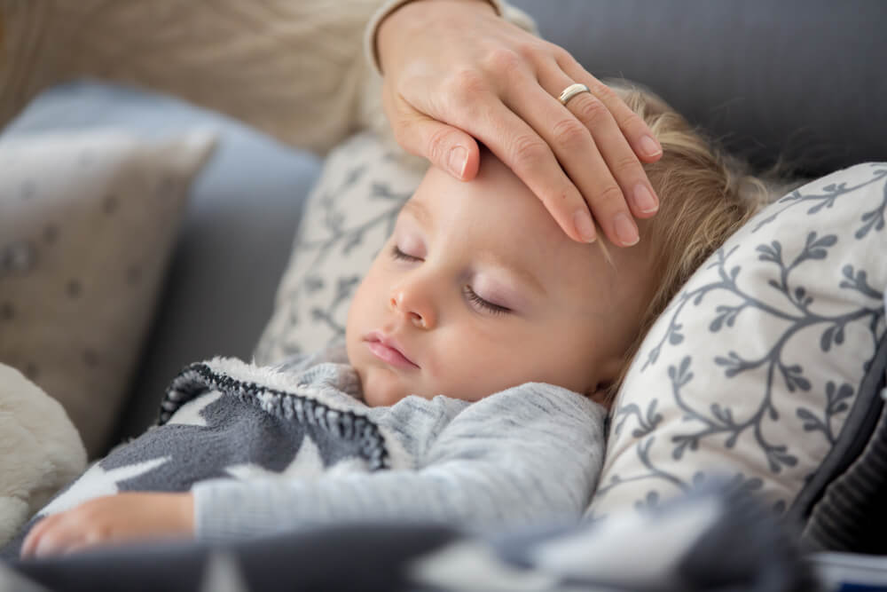 Toddler boy lying on the couch in living room with a fever, mom cheching his temperature