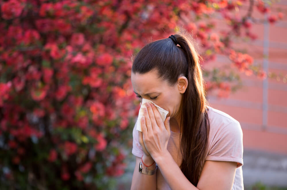 Young Pretty Woman Sneezing in Front of Blooming Tree