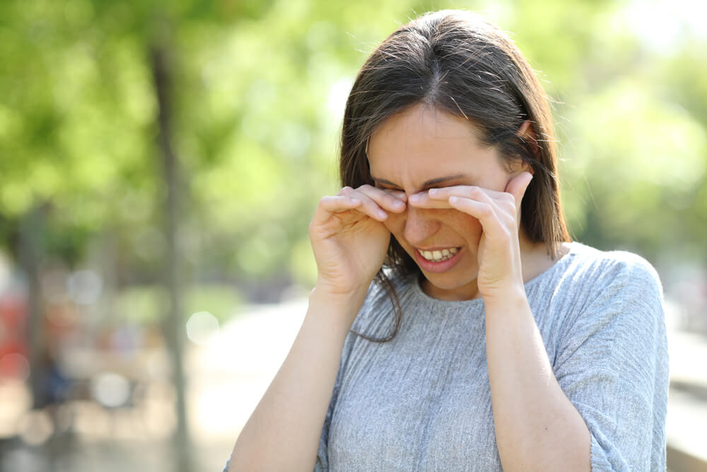 Disgusted Woman Rubbing Her Eyes Standing Outdoors in a Park