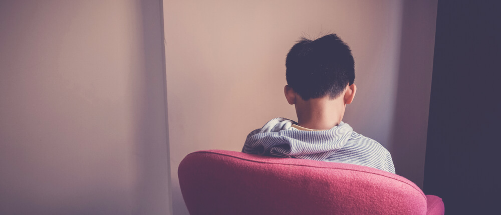 Sad Preteen Boy Sitting Alone in Chair Facing Wall