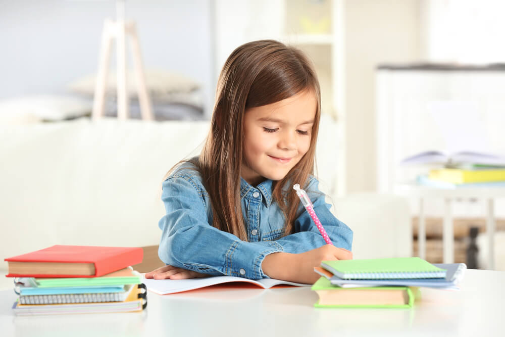 Little Girl Writing Something in Copybook and Sitting at Table
