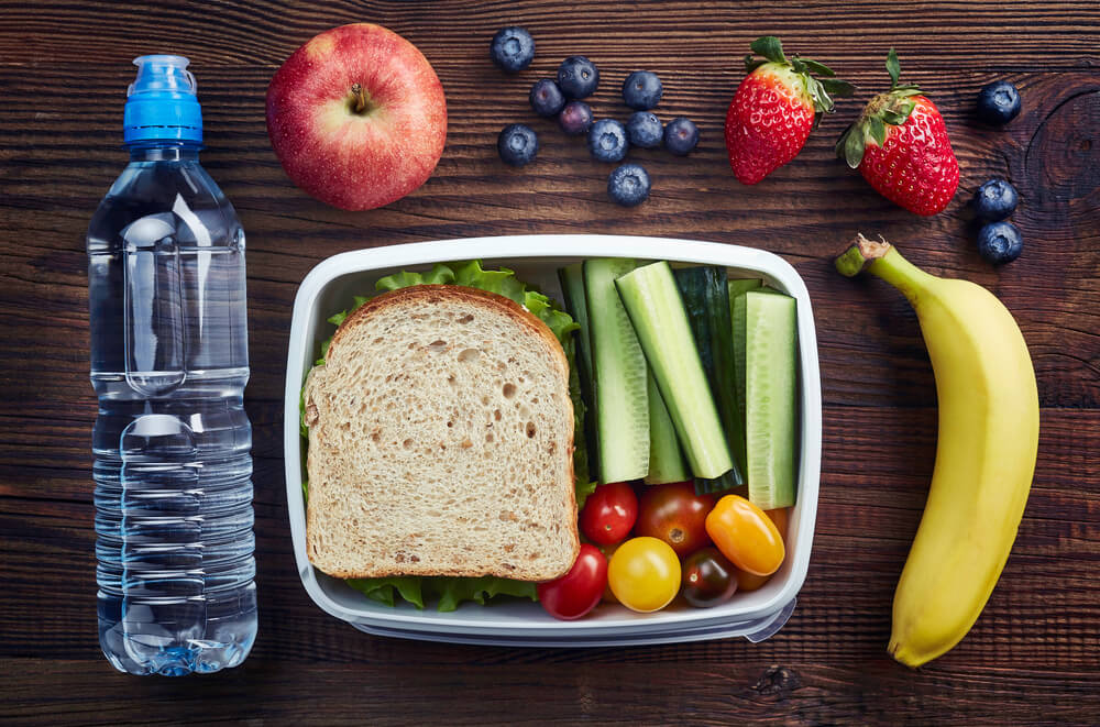 Healthy Lunch Box With Sandwich and Fresh Vegetables, Bottle of Water and Fruits on Wooden Background.