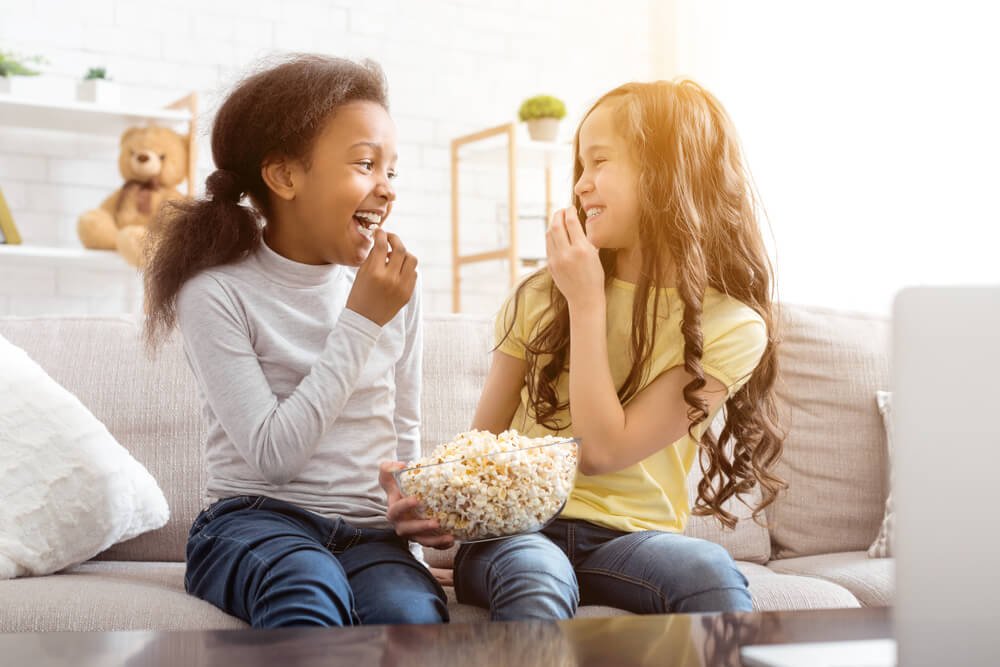 Best Friends Watching Funny Cartoon and Eating Popcorn, Sitting on Sofa at Home