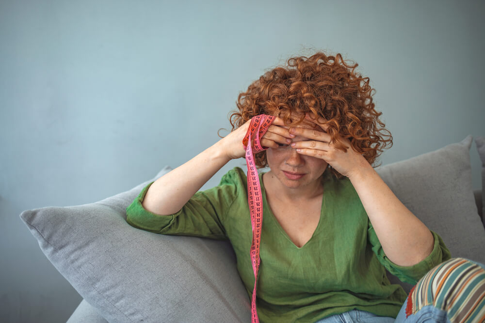 Sad Teen Worried About Appearance Holding a Measure Tape Sitting on a Couch in the Living Room at Home