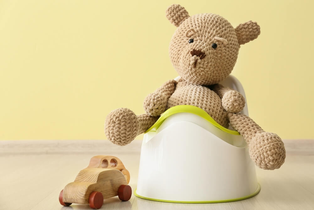 Cute Toy Bear Sitting on Potty and Wooden Car on Floor Near Color Wall