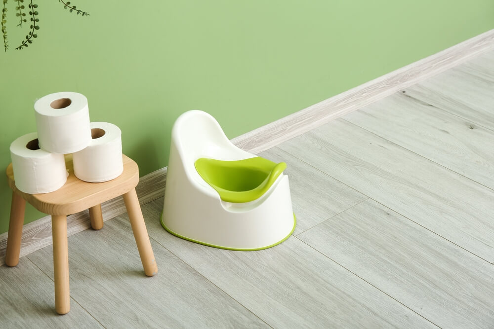 Stool With Toilet Paper Rolls and White Potty on Grey Wooden Floor Near Color Wall