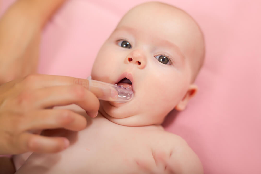 Mother Cleaning Baby`s Mouth With Special Fingertip Brush for Children 