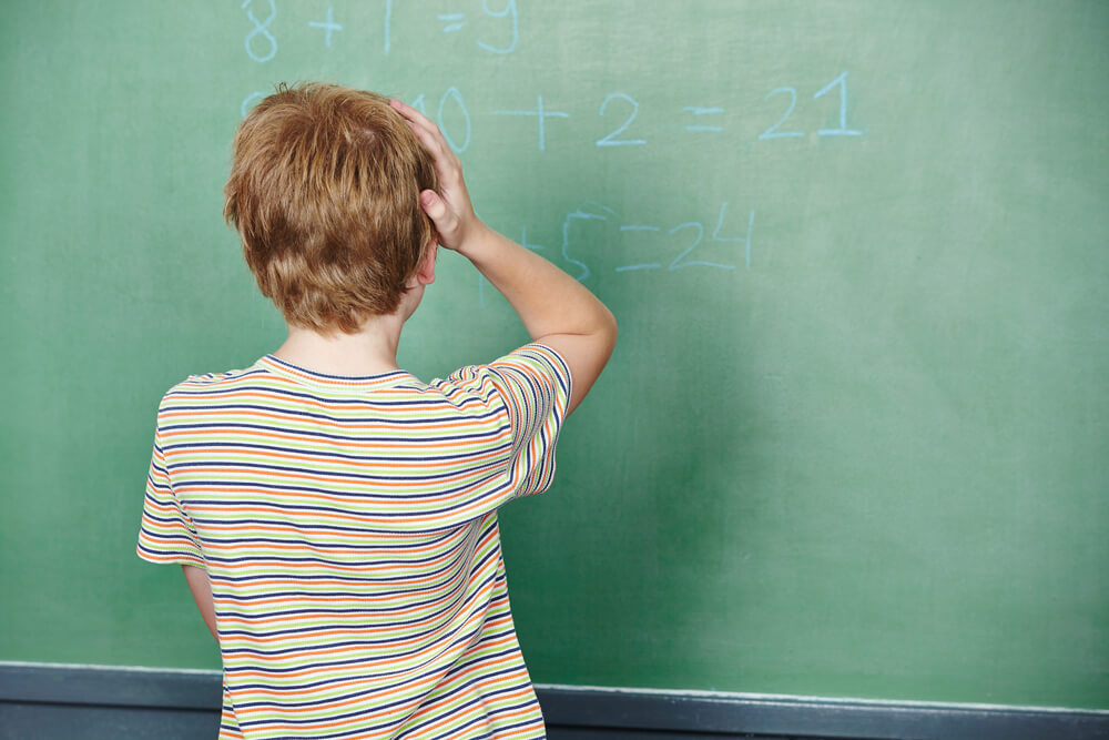 Child Standing in Class in Front of Chalkboard and Thinking About Solution