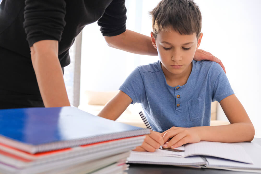 Kid Sitting at the Table With Many Books Notebooks and Doing Homework