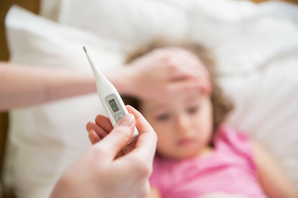 Sick Child With High Fever Laying in Bed and Mother Holding Thermometer. Hand on Forehead.