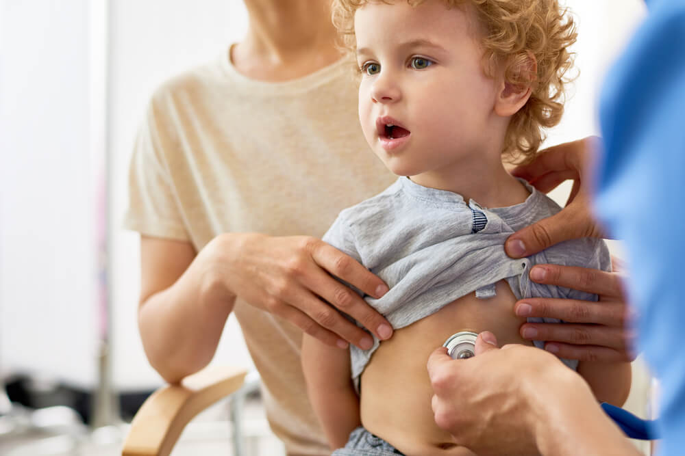 Portrait of Cute Curly Boy Sitting on Mothers Lap During Medical Checkup, Unrecognizable Doctor Listening to Child’s Heartbeat With Stethoscope