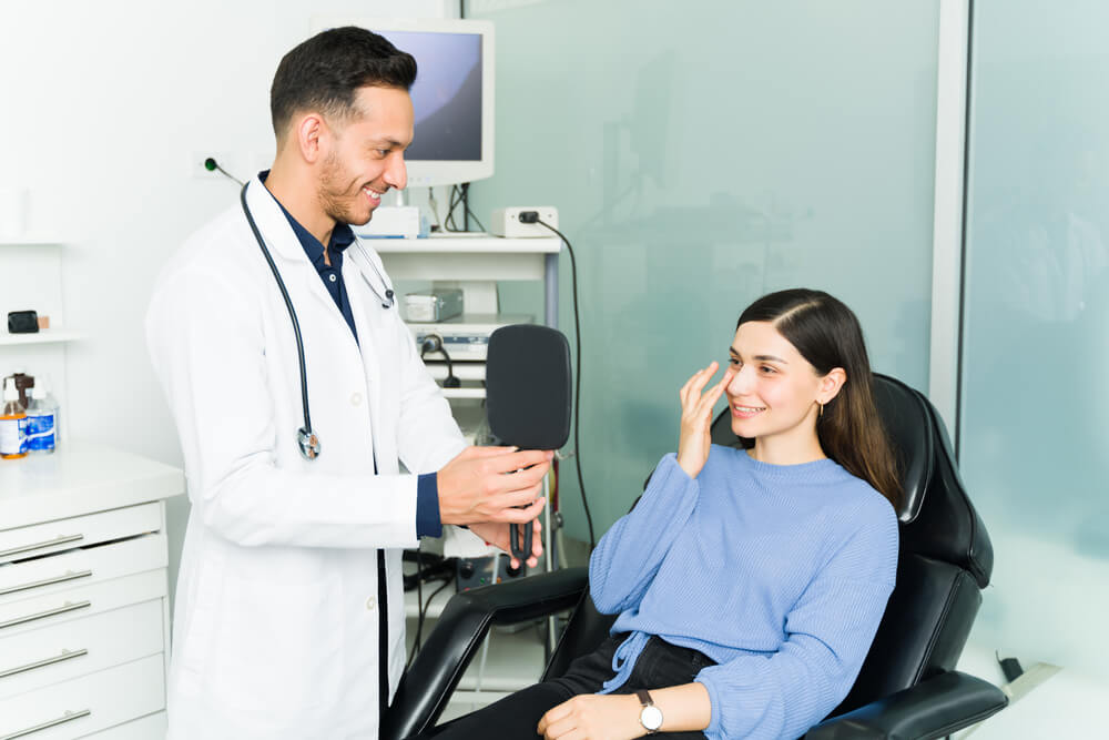 Happy Male Otolaryngologist Holding a Mirror to a Female Patient to Show Her the Results After Her Surgery for a Deviated Septum