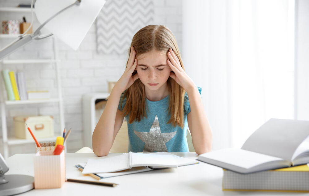 Teenage Girl Suffering From Headache While Doing Homework at Table Indoors