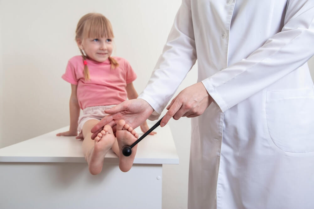 Doctor neuropathologist checks the plantar reflex on the leg of a little girl