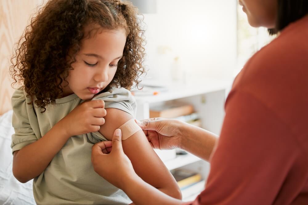 Doctor applying plaster on girl after an injection at health centre.