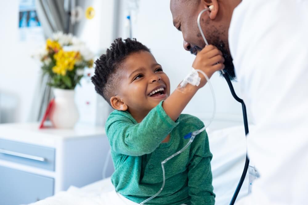Laughing boy patient taking male doctor's stethoscope in hospital.