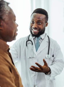 Staying-informed-and-managing-everyday-illnesses Male doctor in a white coat with a stethoscope talking and smiling at a patient.